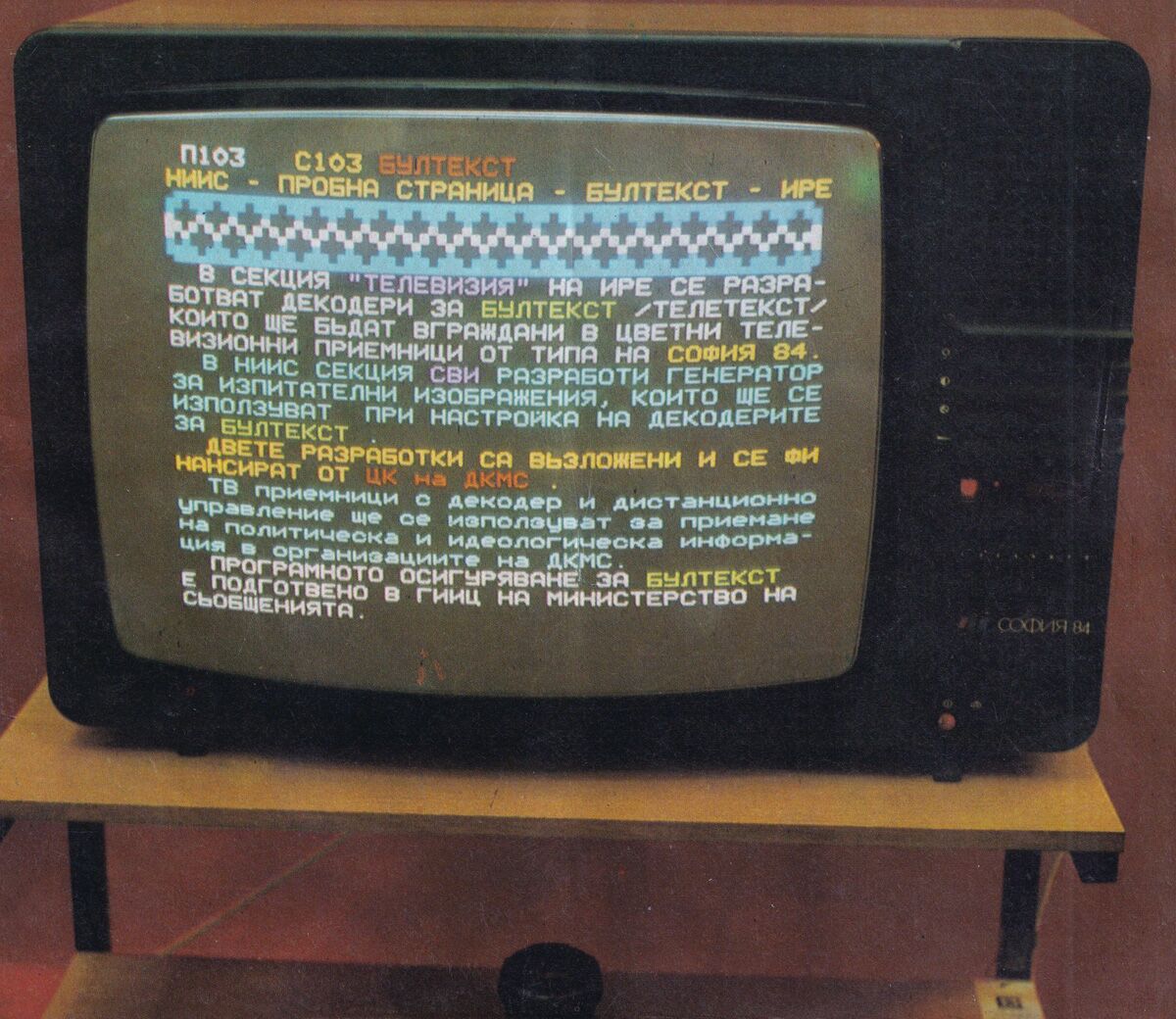 Televizor color din anii 1980, pe un suport de lemn. Pe ecran, o pagină de test a teletextului bulgăresc, scrisă în chirilică.